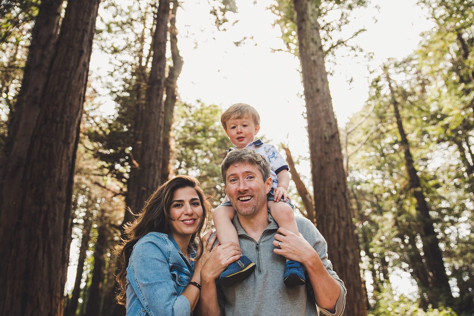 Toddler poses on dads shoulders while mother and father smile at the camera Lovers Lane San Francisco