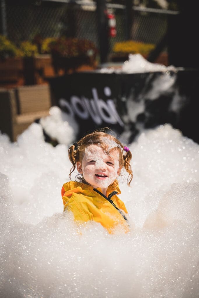 Portrait of a baby girl playing in foam at a foam party in San Francisco organized by Oogubi events and photographed by Mini Anna Photography