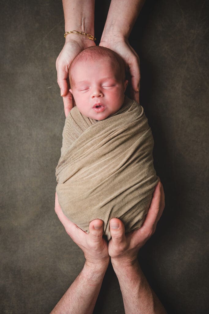 Parents hands pose with swaddled newborn in earth tone linens