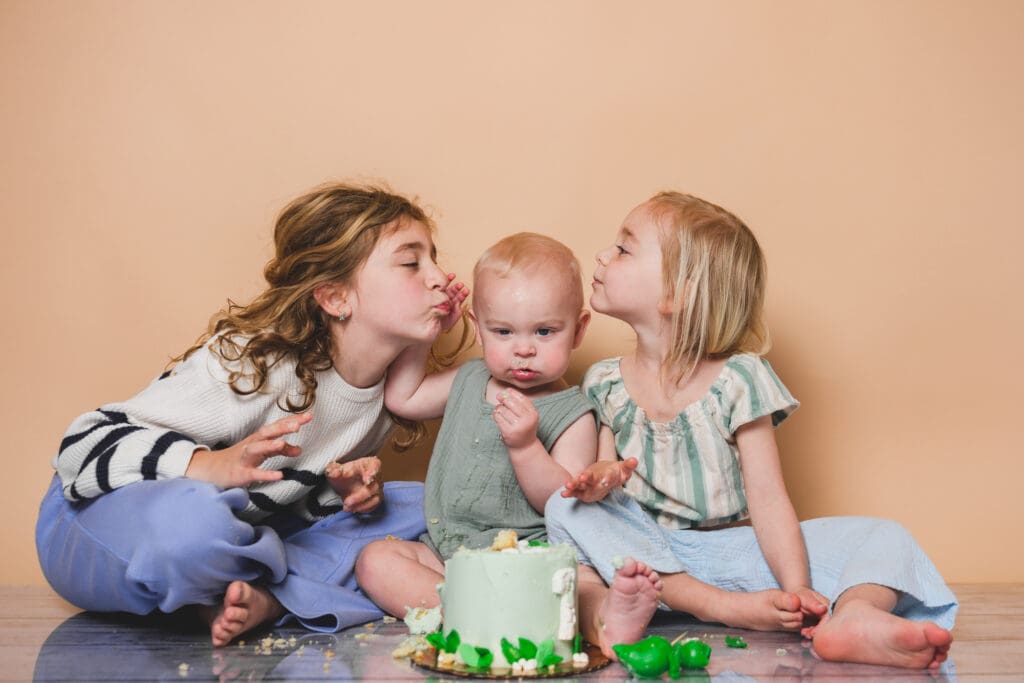 Sisters share kisses while baby shares the cake
