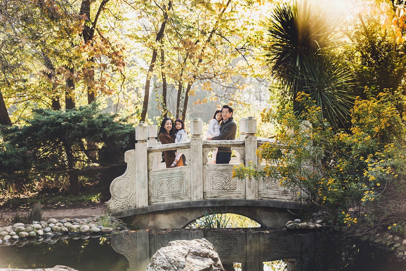 Playful family photo session at Blue Heron Lake in Golden Gate Park with water views, a cute white bridge and tree line paths. 