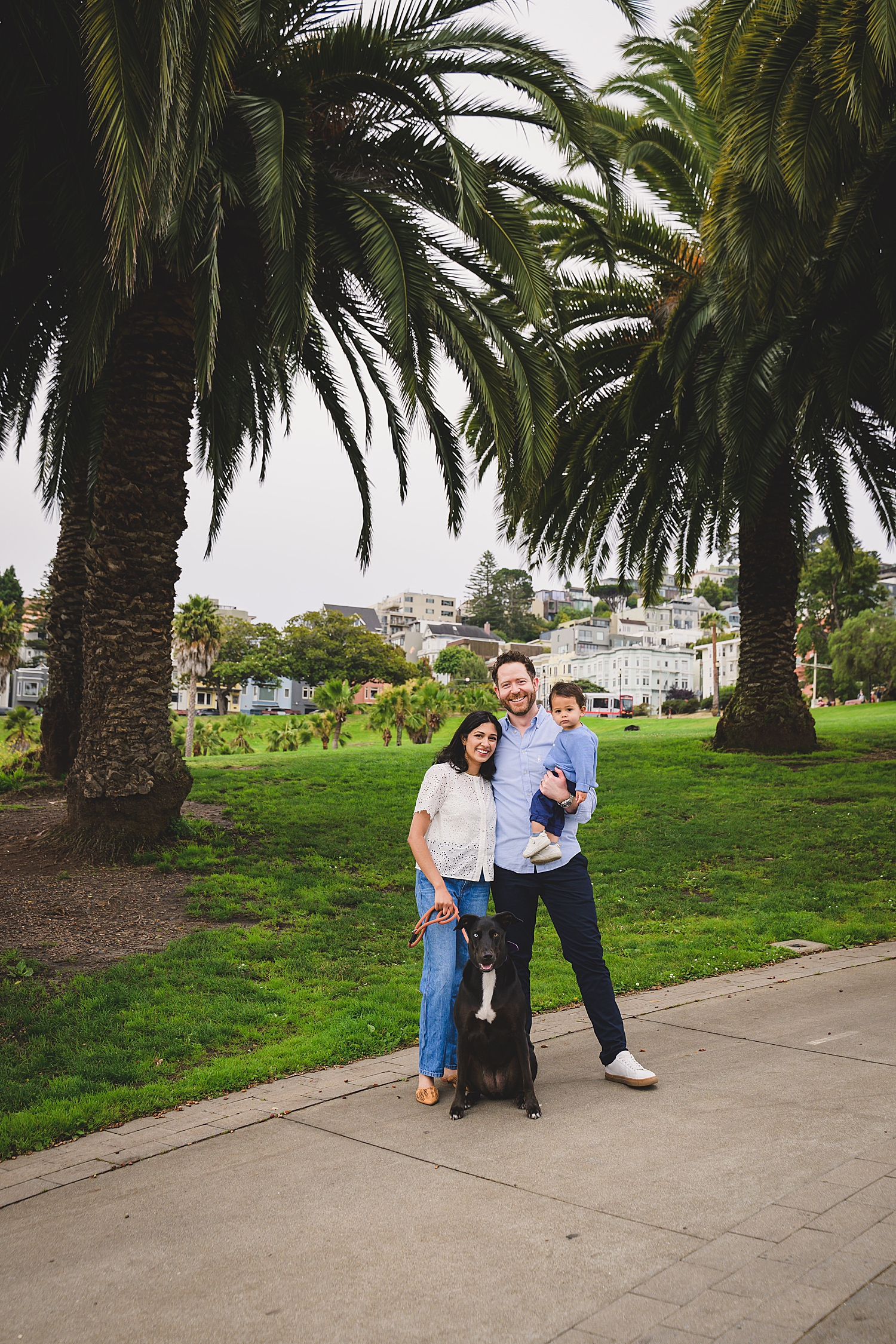 family of three stands with their dog under palm trees showing what to wear for family photos